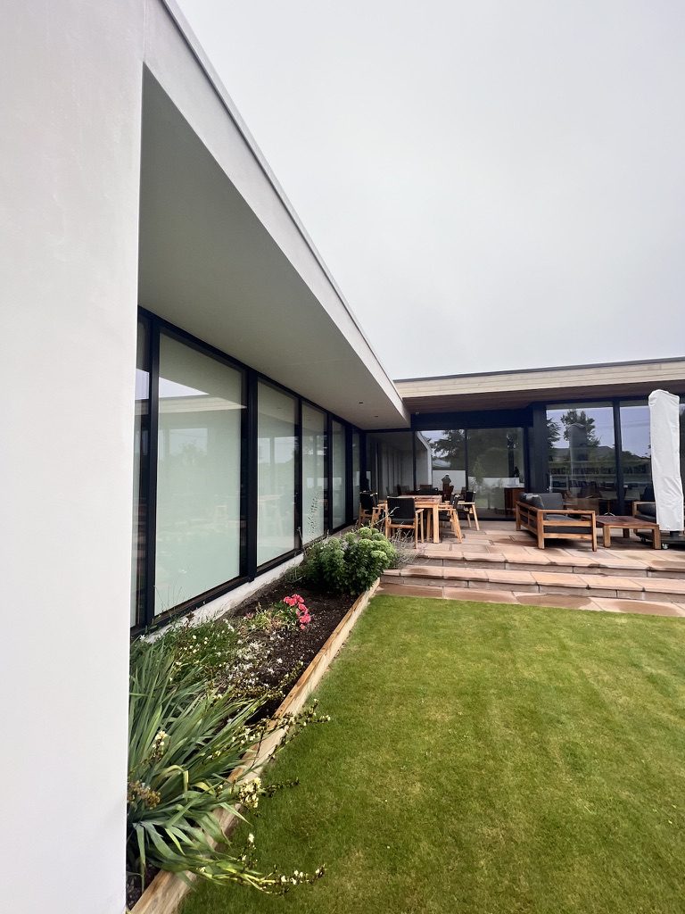 Lawn and garden beside full-height black-framed glazing and covered outdoor dining