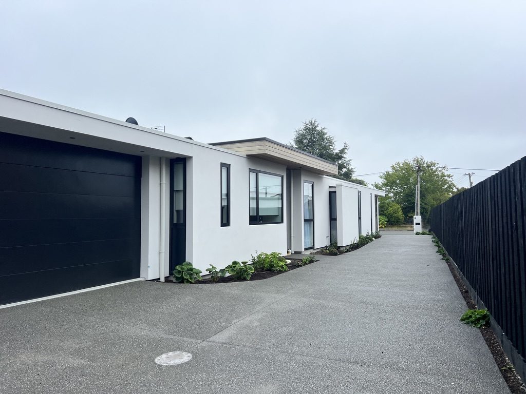 Completed home in Wai-iti, Fendalton: white plaster exterior, black garage door and exposed-aggregate driveway