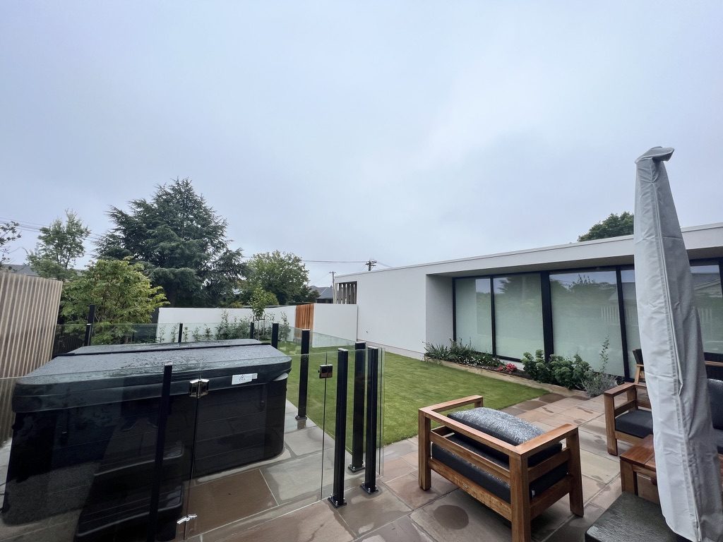 Paved outdoor living area with spa pool, glass fencing and lawn